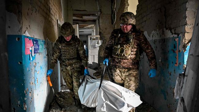 Ukrainian servicemen carry a plastic bag containing the body of a killed Russian soldier found in a destroyed hospital building of the liberated village of Petropavlivka near Kupiansk, Kharkiv region on December 15.