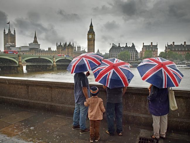 London, UK -July 12th 2016:Tourists with British English flag union jack umbrellas during a London summer rainstorm overlooking the river Thames, Houses of Parliament and Big Ben in Westminster. A dark cloudy typical summer day with rain