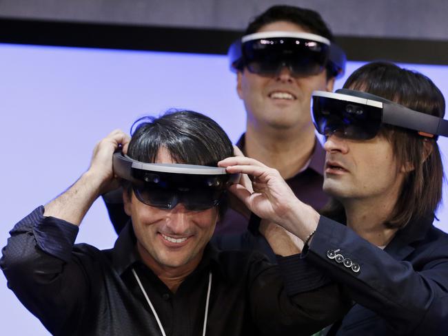 Microsoft's Joe Belfiore, left, smiles as he tries on a "Hololens" device with colleagues Alex Kipman, right, and Terry Myerson following an event demonstrating new features of Windows 10 at the company's headquarters on Wednesday, Jan. 21, 2015, in Redmond, Wash. Executives demonstrated how they said the new Windows is designed to provide a more consistent experience and a common platform for software apps on different devices, from personal computers to tablets, smartphones and even the company's Xbox gaming console. (AP Photo/Elaine Thompson)