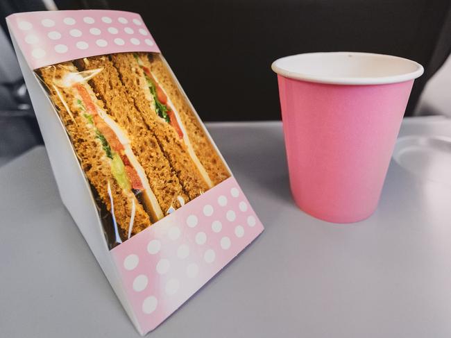 One appetizing sandwich with tuna, tomatoes and a paper glass of tea lie on a table on the plane, close-up side view.