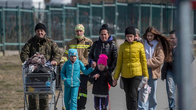 A Polish serviceman, left, helps Ukrainian refugees to cross the Ukrainian border with Poland in 2022. Picture: AFP