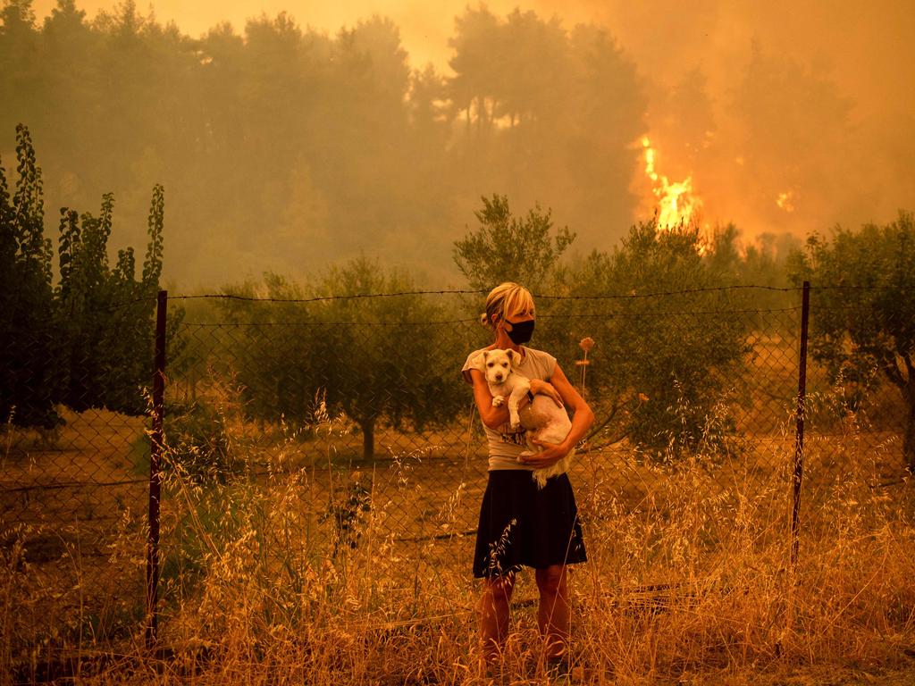 A woman holds a dog in her arms as forest fires approach the village of Pefki on Greece's second largest island. Picture: Angelos Tzortzinis / AFP