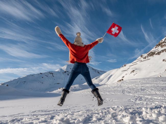 Happy woman with Swiss flag jumping in the air, snowy mountains in winter