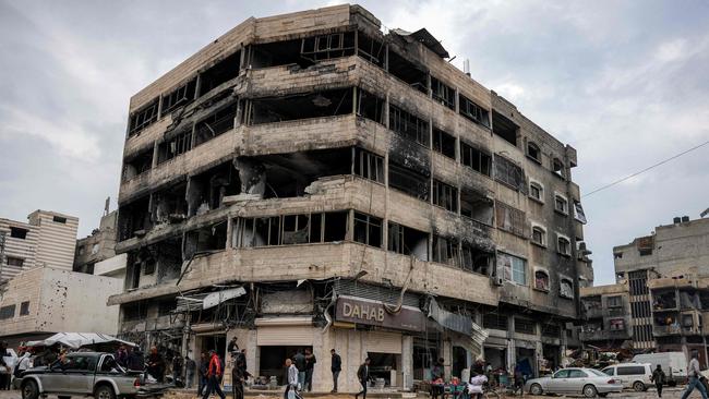 People walk along a flooded street by a heavily-damaged building in the north of Gaza City on February 10, 2025 amid the current ceasefire deal in the war between Israel and Hamas. (Photo by BASHAR TALEB / AFP)