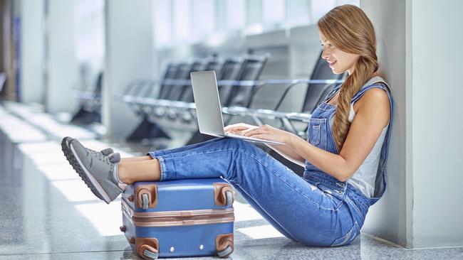 Shot of a young woman using a laptop while sitting on the floor in an airport