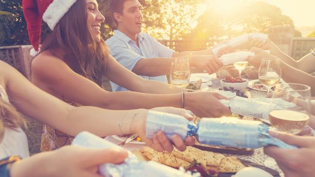 Group of people pulling Christmas crackers. There is food on the table outdoors in a December Summer. There is Cheese and wine. low angle view. Some people are wearing Santa hats