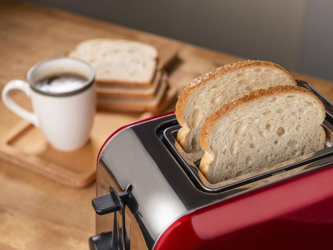 On the kitchen table is a red toaster and a cup of coffee.