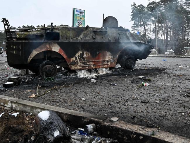 TOPSHOT - Armed man walks past a burned armoured personnel carrier (APC) BTR-4 on a check-point in the city of Brovary outside Kyiv on March 1, 2022. - Russian troops will carry out an attack on the infrastructure of Ukraine's security services in Kyiv and urged residents living nearby to leave, the defence ministry said on March 1, 2022. (Photo by Genya SAVILOV / AFP)