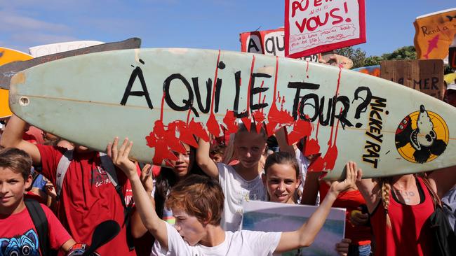 Youths display a surfboard bearing a slogan which translates as "Whose turn next?" and a placard which translates as "It could be you!" as they join a demonstration in Saint-Leu de la Réunion on April 19, 2015 calling for action in the wake of a rise in shark attacks and a day after a 13 year old surfer was killed by a bull shark. Reunion, once a haven for surfers from around the world, has become a deadly black spot for the sport now plunged into even deeper mourning after a shark mauled Elio Canestri to death. The 13-year-old, one of the Indian Ocean island's most promising young surfers, was killed after he ignored an official ban and hit the waves with friends. AFP PHOTO / RICHARD BOUHET