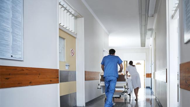 Rearview shot of hospital staff wheeling a patient in a gurney down a corridor