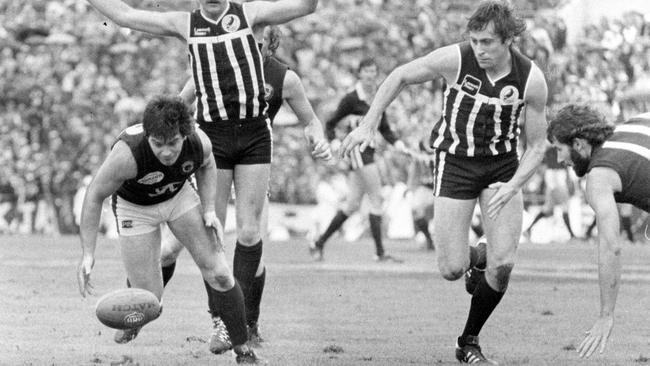 Port Adelaide vs. South Adelaide SANFL Grand Final match at Football Park, West Lakes, 30 Sep 1979. South's Phil Collins bends low and puts his body over the ball in an attempt to clear. Magpie Paul Belton keeps his hands high as he follows Collins and teammate Peter Hofner keeps pace.