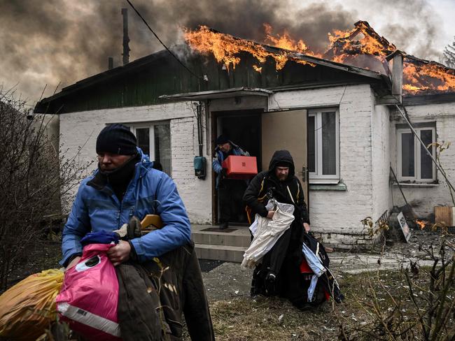 TOPSHOT - People remove personal belongings from a burning house after being shelled in the city of Irpin, outside Kyiv, on March 4, 2022. - More than 1.2 million people have fled Ukraine into neighbouring countries since Russia launched its full-scale invasion on February 24, United Nations figures showed on March 4, 2022. (Photo by Aris Messinis / AFP)