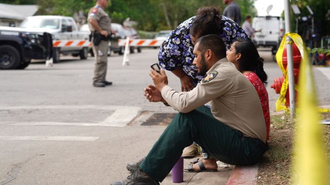A sheriff and two women in tears as they sit on a kerb outside the school. Picture: Allison Dinner/AFP via Getty Images