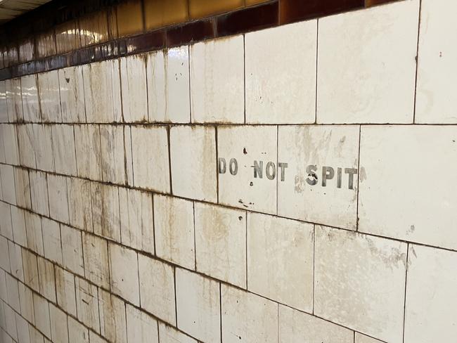 A faded ‘do not spit’ sign peeks through smears of brown grime.