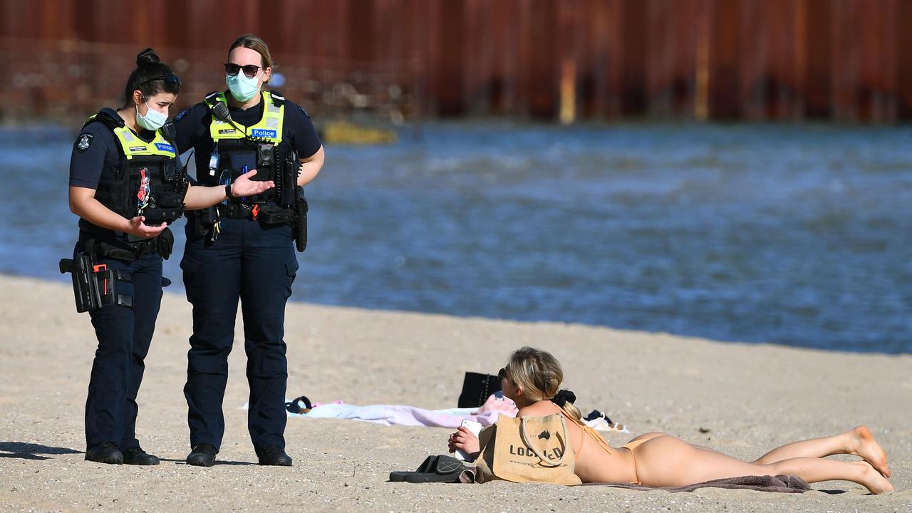 Police speak to a woman laying on the beach at St Kilda. Picture: William West/AFP