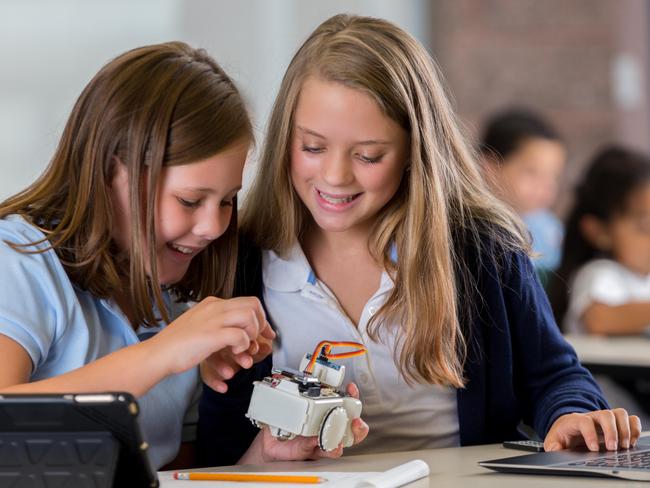 Junior high school girls are studying robotics in private school STEM class. Preteen classmates are examining and programming a small robot, while using digital tablets, laptops, and other modern technology.