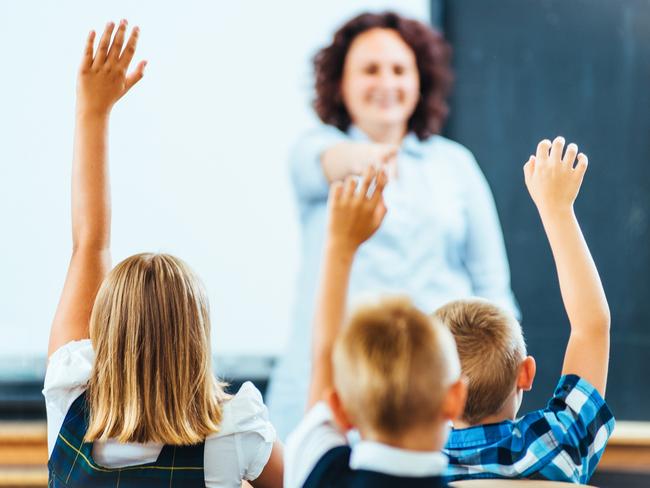 Primary School children raising hands in Classroom