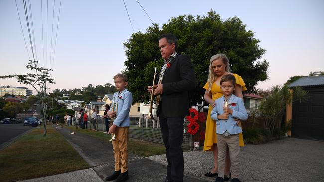 Alastair Tomkins, joined by his wife Katie and their sons Hugo, 9, (left) and Lyndon, 6, stand in silence after playing The Last Post in their driveway, at dawn, as neighbours stand outside their homes to commemorate Anzac Day in Brisbane, Saturday, April 25, 2019. Anzac Day is a national day of remembrance to commemorate the service and sacrifice of Australian and New Zealand service men and women. Due to COVID-19 restrictions marches and commemorative services have been banned for the first time in more than a century. (AAP Image/Dan Peled) NO ARCHIVING