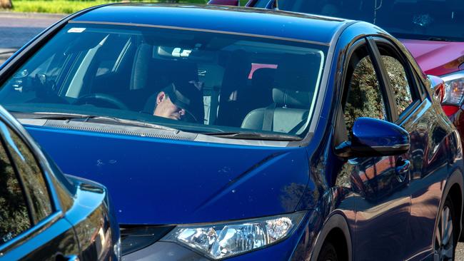 A parent in Melbourne’s north, who has arrived hour early to get a park, sleeps in his car while waiting for the bell to go. Picture: Jay Town