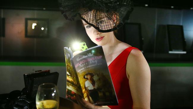 Annabel Pike browses the form guide using a torch after a power outage at Eagle Farm on Tuesday. Picture: Liam Kidston