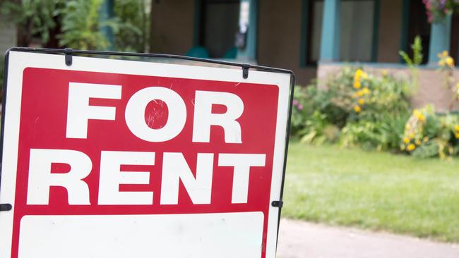 A blank red and white for rent sign is posted in the front yard of a home.