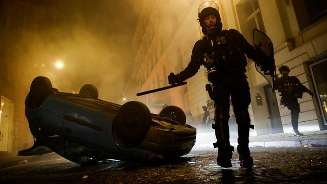 French riot police walk next to an overturned vehicle in Paris. Picture: Reuters