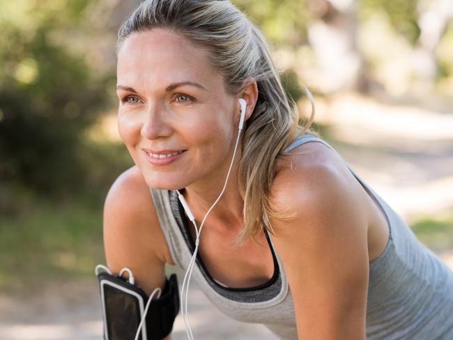 Portrait of athletic mature woman resting after jogging. Beautiful senior blonde woman running at the park on a sunny day. Female runner listening to music while jogging.