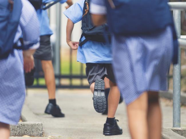 School children running away. They are wearing uniforms and carrying backpacks. They are having a race. Multi ethnic group with Asian, Caucasian and Aboriginal children. Rear view