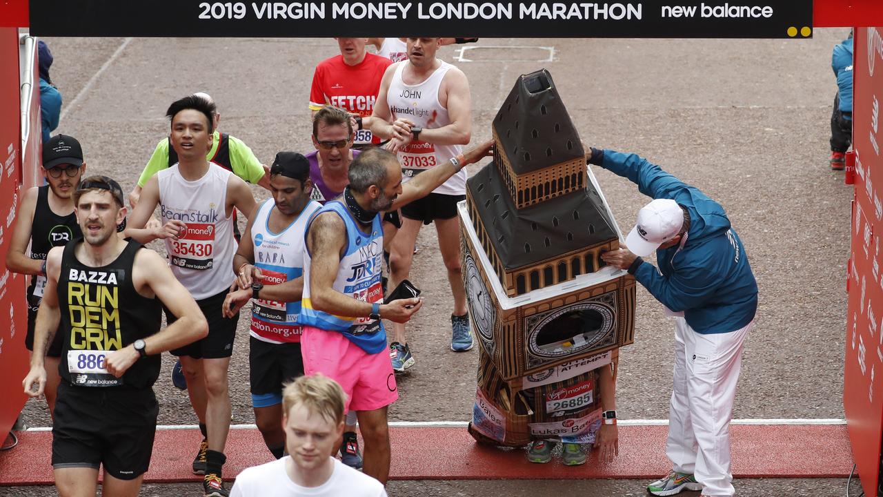 A steward and another runner help Lukas Bates to get the top of his costume under the structure at the top and cross the finish line. Picture: AP