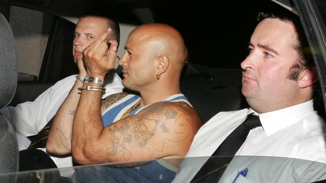 Binse sits between two armed offenders squad detectives and greets the media after his arrest over the Spearmint Rhino visit.