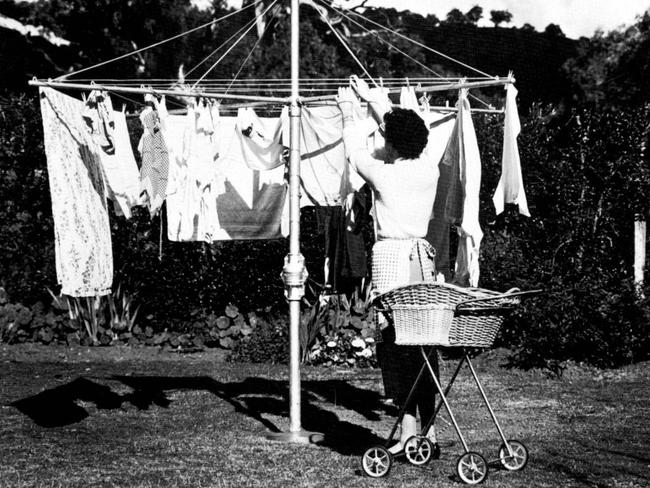 A woman hangs out her washing on an early-model Hills hoist.