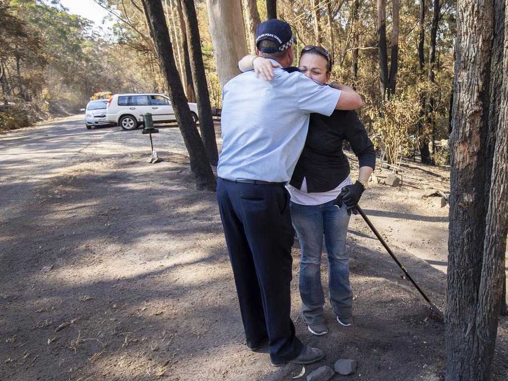 Sara Barnard is comforted by police officer Darren Wood in front of her home, which was spared in the blaze. Picture: AAP.