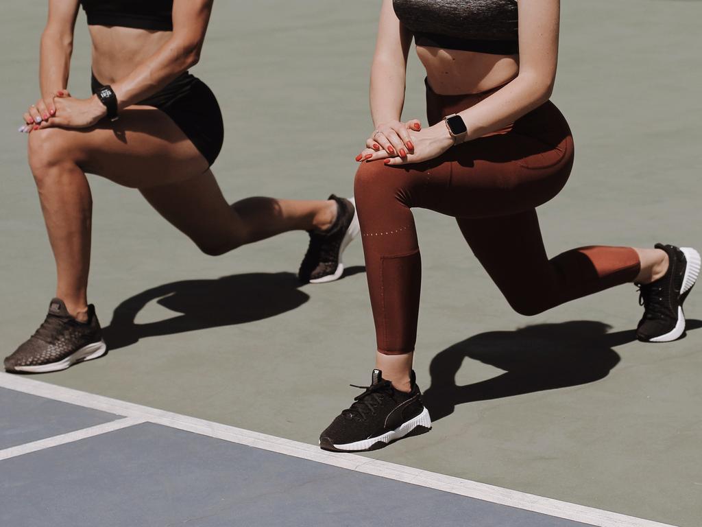 Two women lunging in activewear on a tennis court