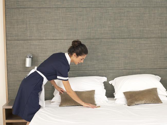 Generic image of a housekeeper making a bed in a room of a hotel.