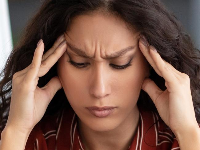 Tired From Work. Portrait of exhausted stressed young woman suffering from headache, touching and massaging her forehead and temples, sitting at desk near whiteboard, thinking about problems