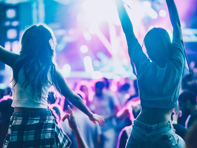 Back view of carefree women having fun while being on man's shoulders during music festival.