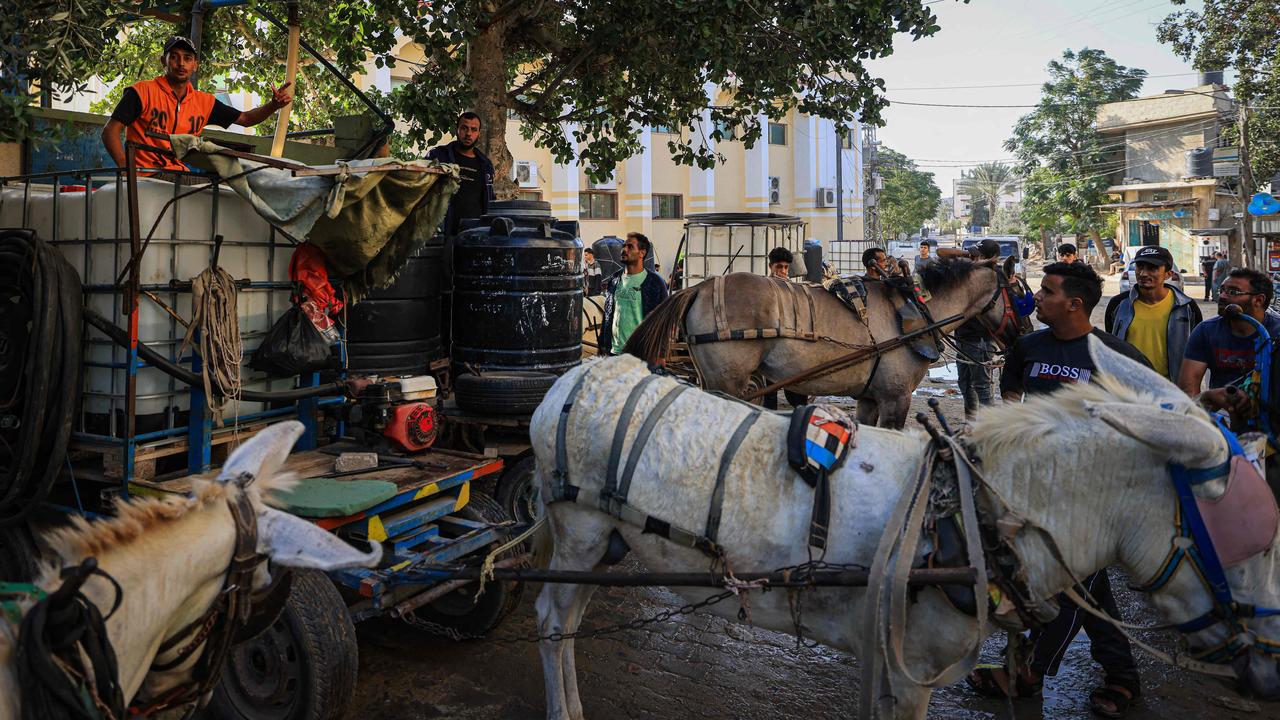 Palestinians gather next to donkey-drawn carts loaded with water tanks for sale, as drinking water supplies become increasingly scarce. Picture: AFP