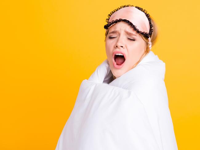 Concept of healthy sleep. Sleepy girl yawning wide open mouth wrapped in blanket and with eyemask on her head isolated on yelow background