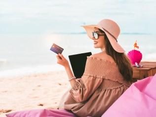 Beautiful asian smile woman relax at beach on summer vacation. Holding credit card with computer. Digital payment concept for shop online and booking hotel when travel. Pattaya, Thailand.