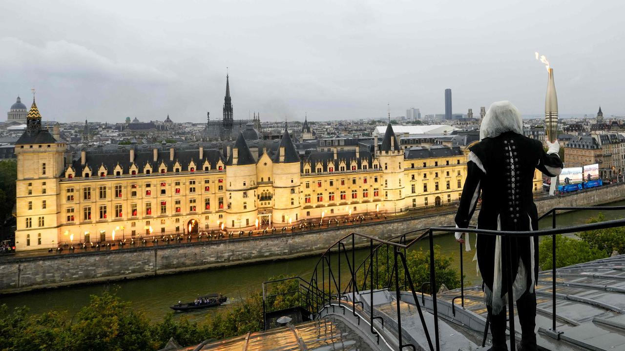 A torchbearer carries the Olympic flame over a building along the Seine. Picture: Bernat Armangue / POOL / AFP