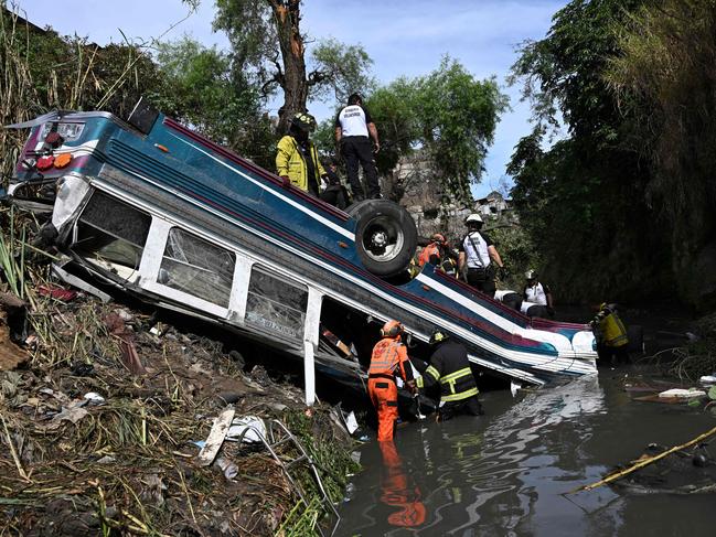 TOPSHOT - Firefighters work at the scene of an accident in which a bus fell down a ravine in Guatemala City on February 10, 2025. More than 50 people were killed on Monday when a bus crashed through a guard rail and plunged into a ravine, rescuers said, one of the worst road accidents in Latin America in years. (Photo by Johan ORDONEZ / AFP)