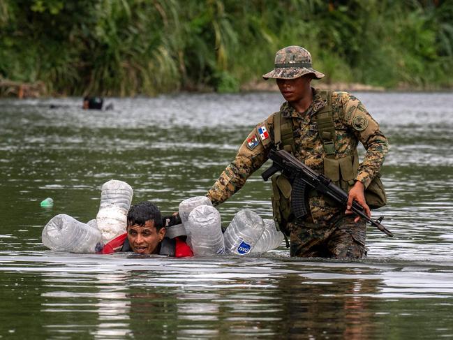 A Venezuelan migrant is helped by a member of Panama's Border Service as he floats using plastic bottles to cross the Turquesa River with an injured knee. More than 390,000 migrants have entered Panama through this jungle so far this year, far more than in all of 2022, when there were 248,000. Picture: Luis Acosta/AFP