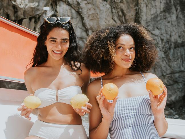 Two beautiful young woman enjoy a risque joke, holding lemons and oranges over their breasts, while making silly faces.