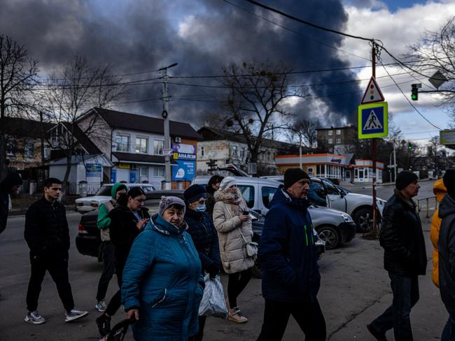 People stand in line in front of a supermarket while smoke billows over the town of Vasylkiv just outside Kyiv. Picture: Dimitar DILKOFF / AFP