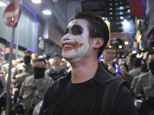 A man wearing Joker face paint stands in front of police officers in riot gear on a street in Hong Kong as the territory slides into recession. Picture: AP Photo/Kin Cheung