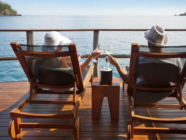 Couple relaxing on sun lounges in an over water bungalow toasting. Picture: iStock