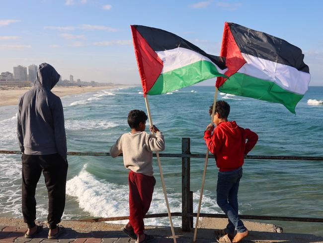 TOPSHOT - Two boys hold Palestinian flags as they arrive to watch Hamas fighters handover an Israeli-American hostage to a Red Cross team in Gaza City on February 1, 2025, as part of the fourth hostage-prisoner exchange. Ranks of Hamas fighters formed up on Gaza's beachfront on February 1 for the handover of an Israeli-American hostage Keith Siegel in a show of force against the dramatic backdrop of breaking waves. (Photo by Omar AL-QATTAA / AFP)