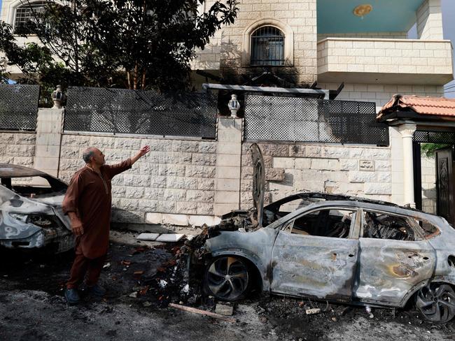 TOPSHOT - A man standing next to burnt cars points at the damage in his house, a day after an attack by Jewish settlers on the village of Jit near Nablus in the occupied West Bank that left a 23-year-old man dead and others with critical gunshot wounds, on August 16, 2024. Negotiators trying to hash out a Gaza ceasefire deal were due to meet for a second day in Qatar on August 16, after the deadly Jewish settler attack on the Palestinian village drew widespread rebuke, including from Israeli officials. (Photo by Jaafar ASHTIYEH / AFP)