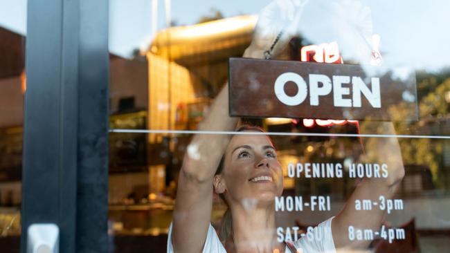 Portrait of a happy business owner hanging an open sign on the door at a cafe and smiling - food and drinks concepts