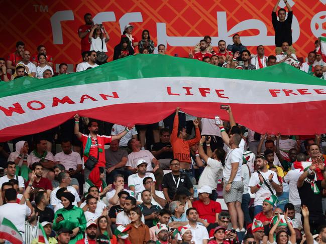 Iran supporters wave their national flag bearing the word "Woman, Life, Freedom" as they cheer during the Qatar 2022 World Cup Group B football match between England and Iran at the Khalifa International Stadium in Doha on November 21, 2022. (Photo by FADEL SENNA / AFP)